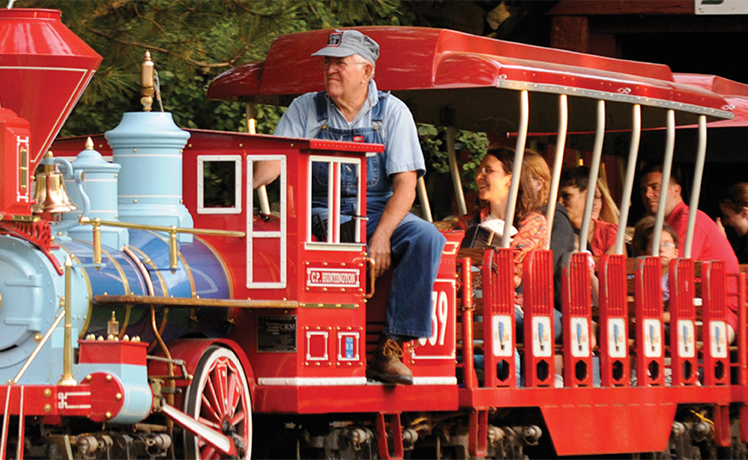 Man driving miniature train with people riding behind him